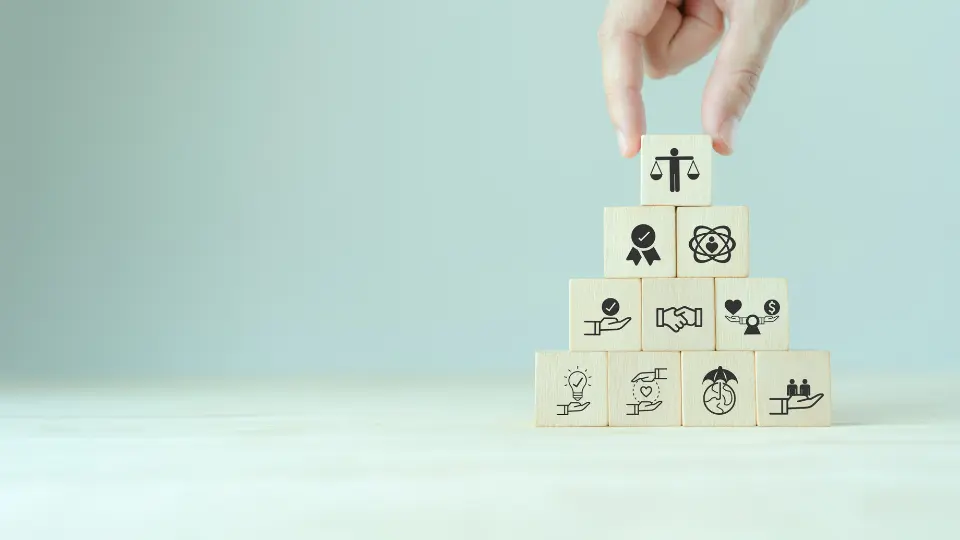 Mão organizando blocos de madeira empilhados com ícones de valores de ética e justiça